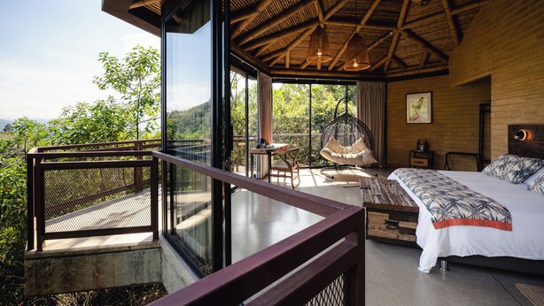 Un dormitorio con una cama grande, una silla colgante y un balcón con vistas al exterior.