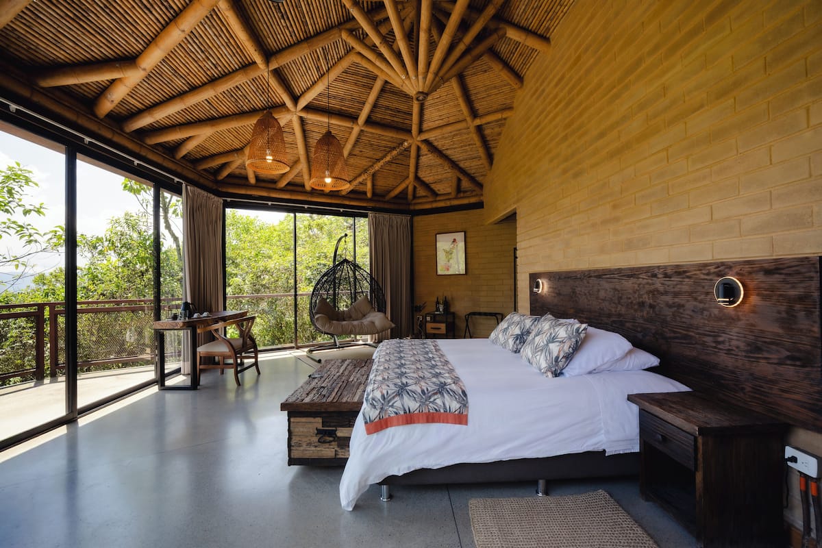A spacious bedroom with a large bed, wooden ceiling, and a balcony with a view of trees.