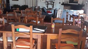 A dining area with wooden tables and chairs, a television, and a window with curtains.