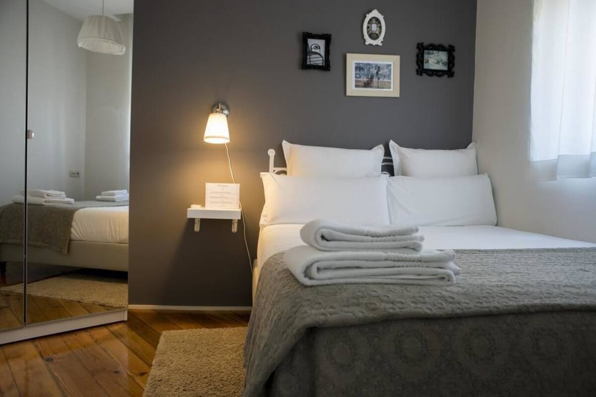 Ein Schlafzimmer mit einem Bett, einem Nachttisch mit Lampe, einem Spiegel und einer Wand mit gerahmten Bildern.