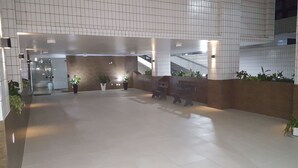 A spacious lobby with tiled flooring, benches, potted plants, and a staircase. - Apartamento em frente a Praia Santos (Santos)