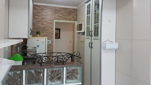 A modern kitchen with white cabinets, a granite countertop, and a built-in oven. - Apartamento em frente a Praia Santos (Santos)