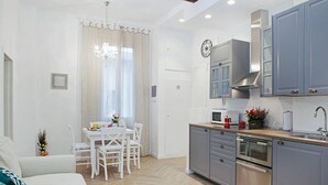 A modern kitchen with grey cabinets, a microwave, and a sink. There is a dining area with a white table and chairs. - Flavourful Flat down Pratello Area - Flat in Bo (Bologna)