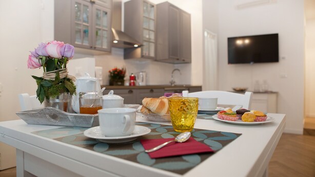 A dining table with a white tablecloth, a vase with pink flowers, a cup of tea, and a plate of pastries. - Flavourful Flat down Pratello Area - Flat in Bo (Bologna)