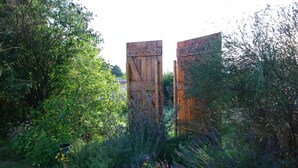 A garden with wooden gates, dense foliage, and a potted plant with purple flowers. - Chambres d'hôtes Lou Cliou (Cliousclat)