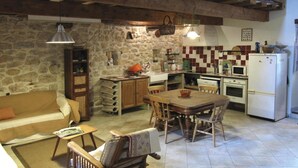 A rustic kitchen with a stone wall, wooden furniture, and basic appliances. - Chambres d'hôtes Lou Cliou (Cliousclat)