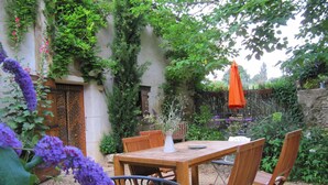A wooden table and chairs in a garden with a stone wall, a wooden fence, and various plants. - Chambres d'hôtes Lou Cliou (Cliousclat)