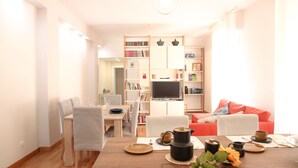 A modern living room with a wooden dining table, chairs, a sofa, and a TV. - Secret Garden Via San Rocco - Flat in Bo (Bologna)