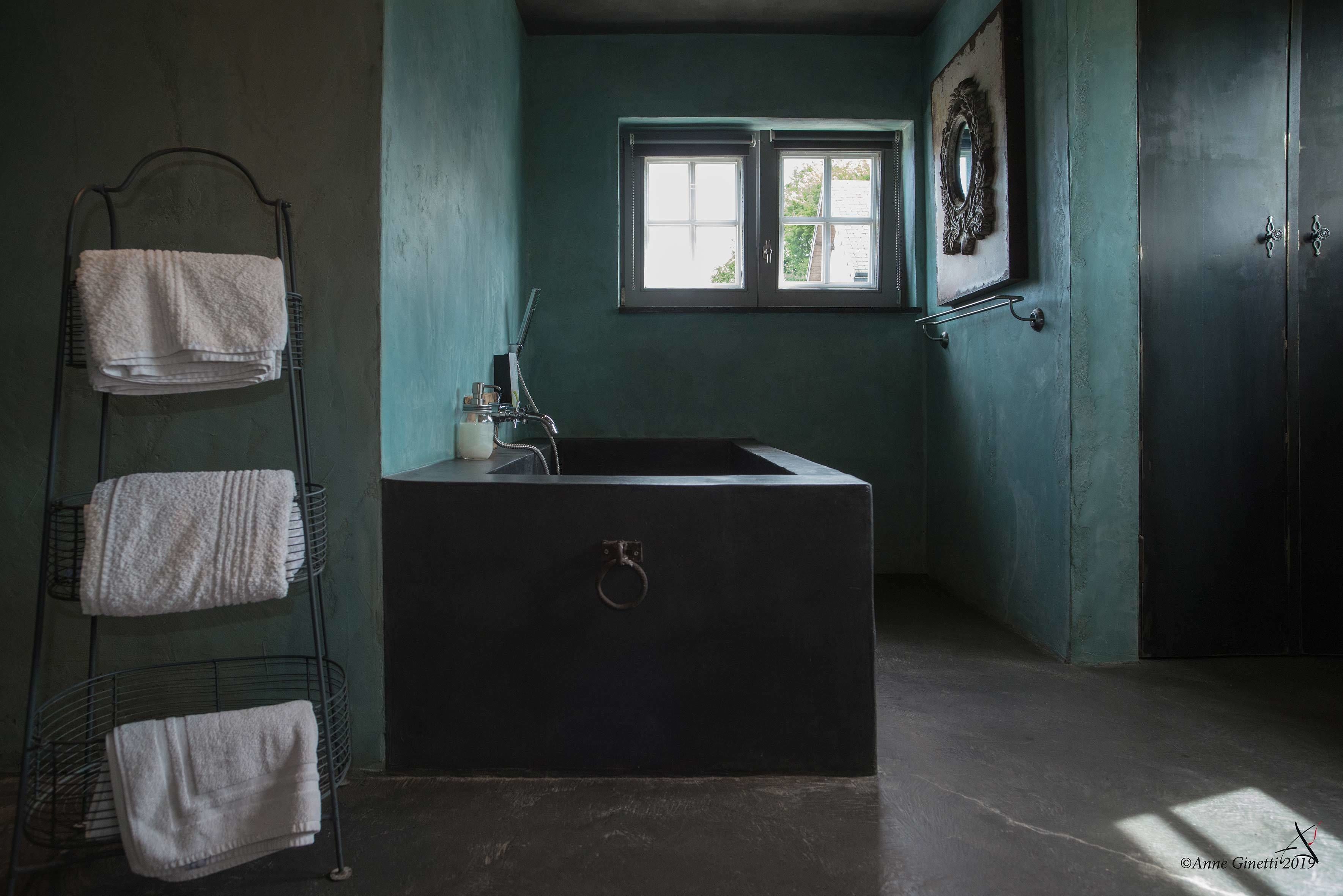 A bathroom with a large bathtub, a towel rack with multiple towels, a window, and a door.