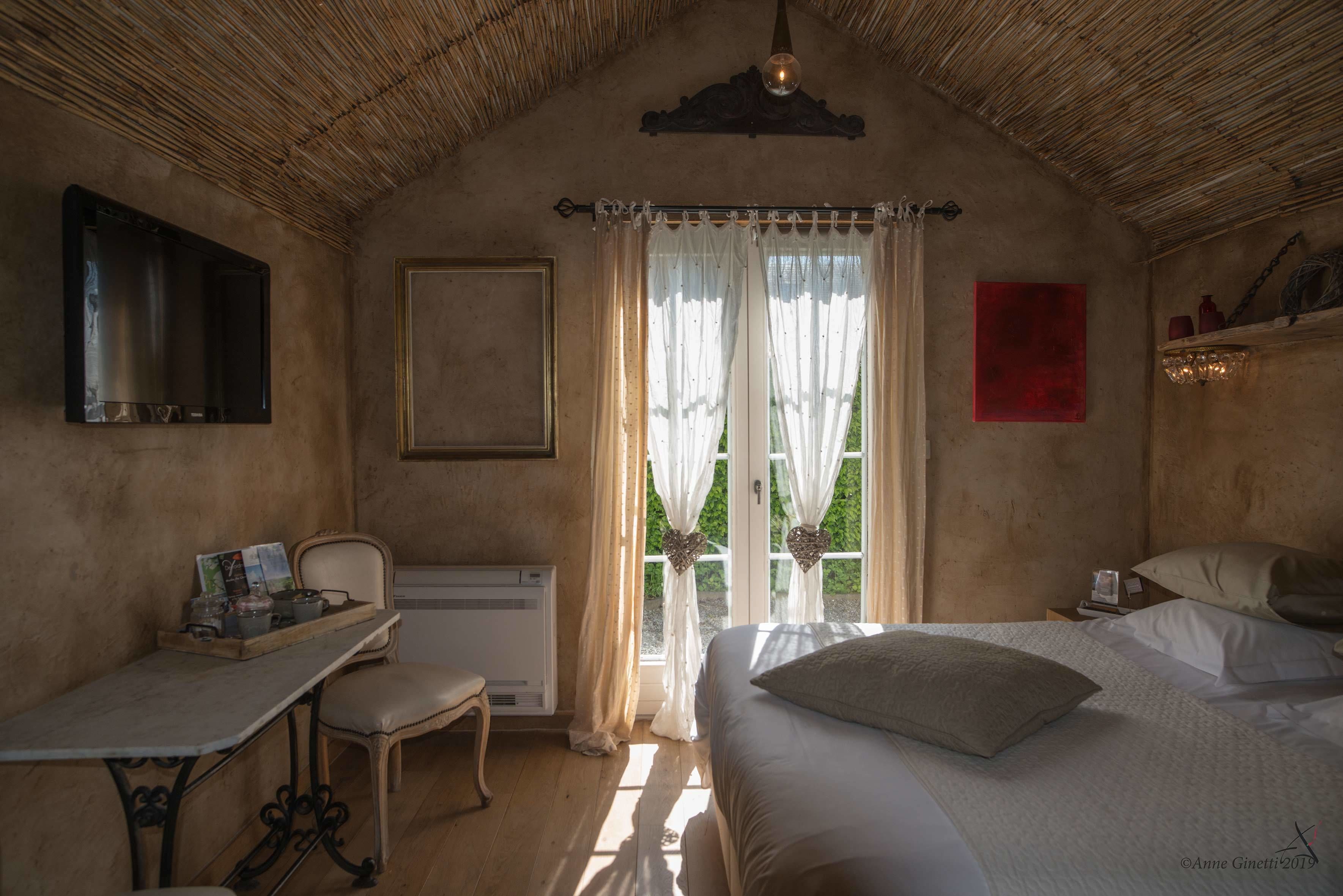 Een knus slaapkamer met een bed, een bureau en een stoel. Er is een raam met gordijnen en uitzicht op groen.