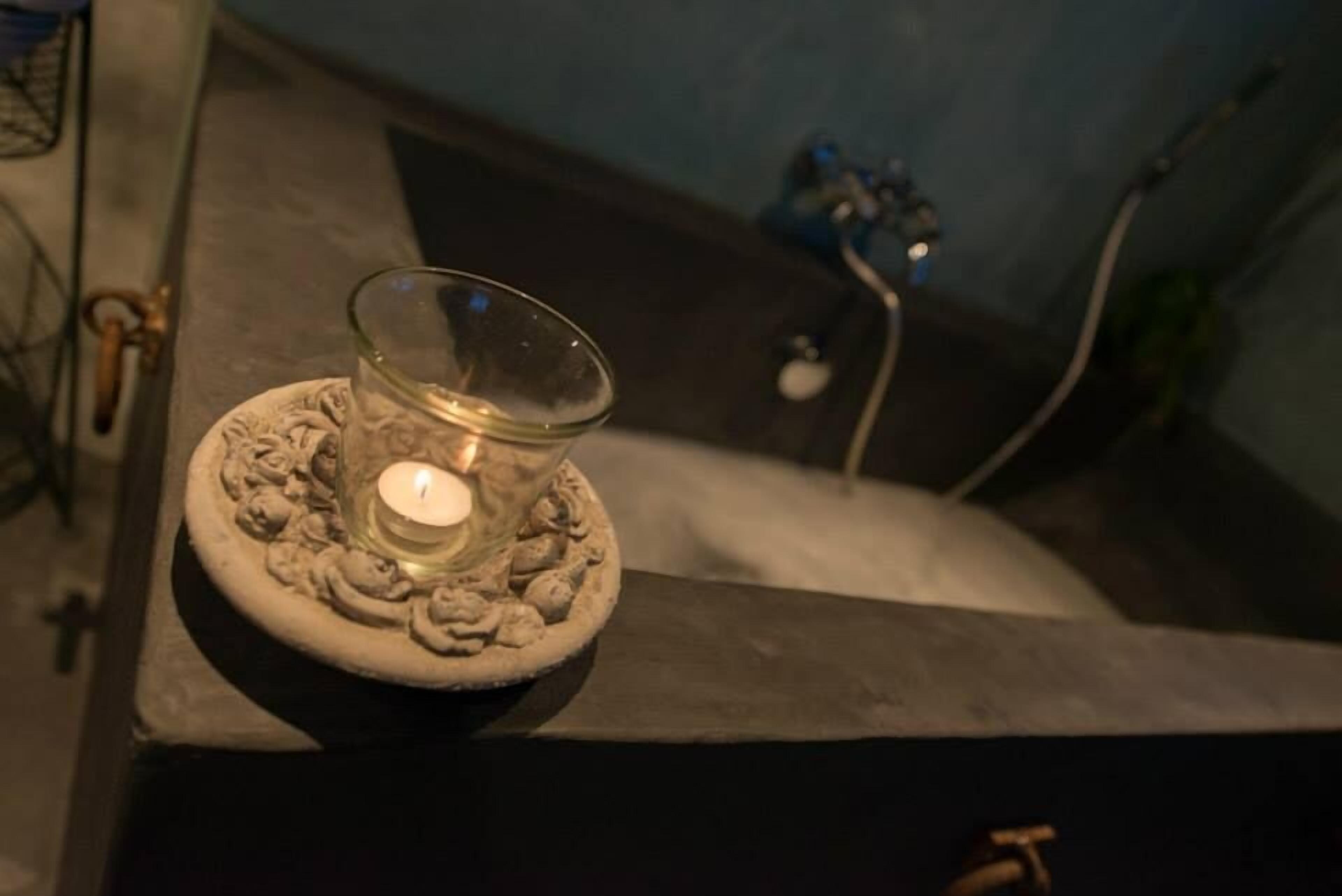 Une bougie dans un porte-bougie en verre, posée sur une surface en pierre.