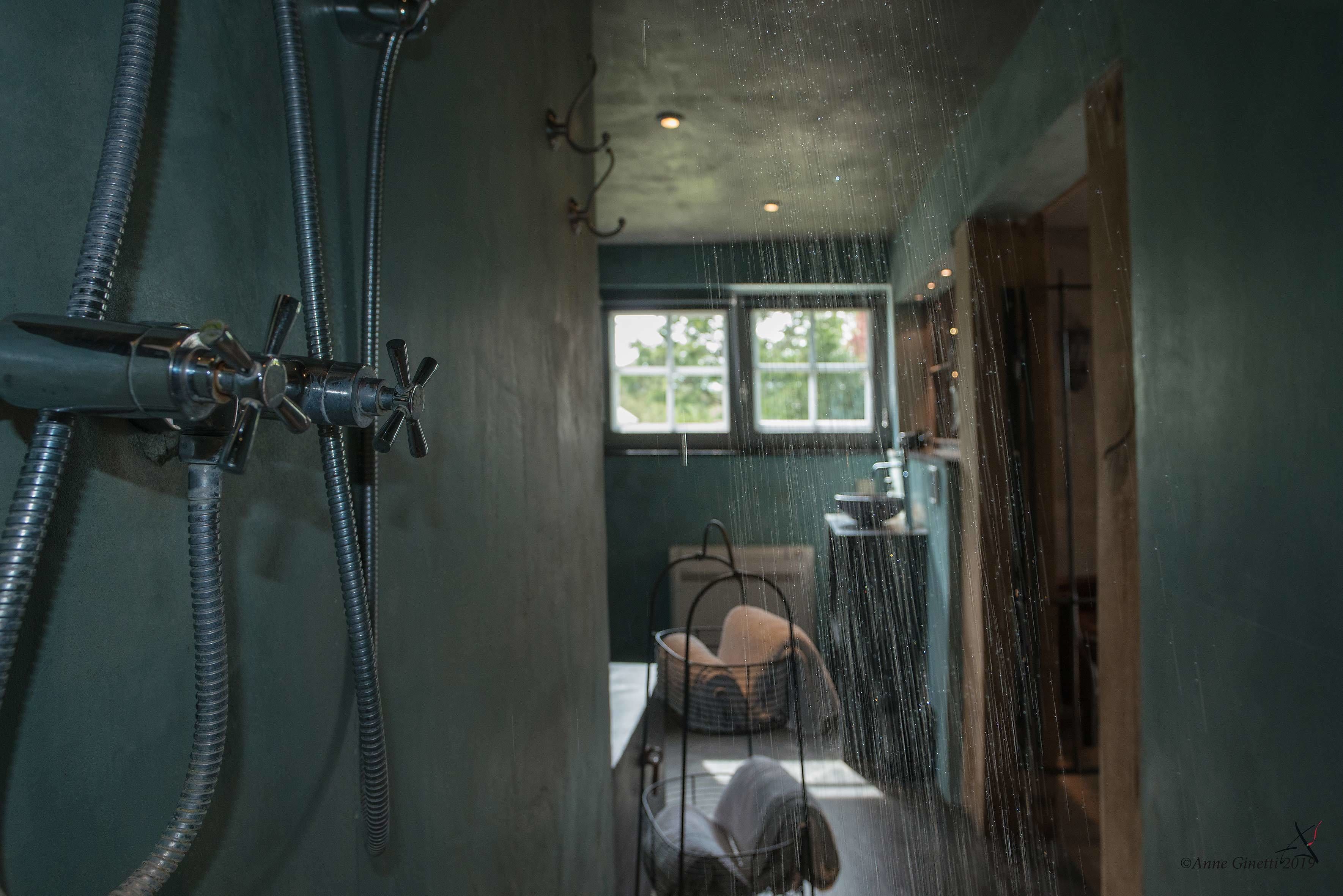 Een badkamer met douche, raam en wastafel.