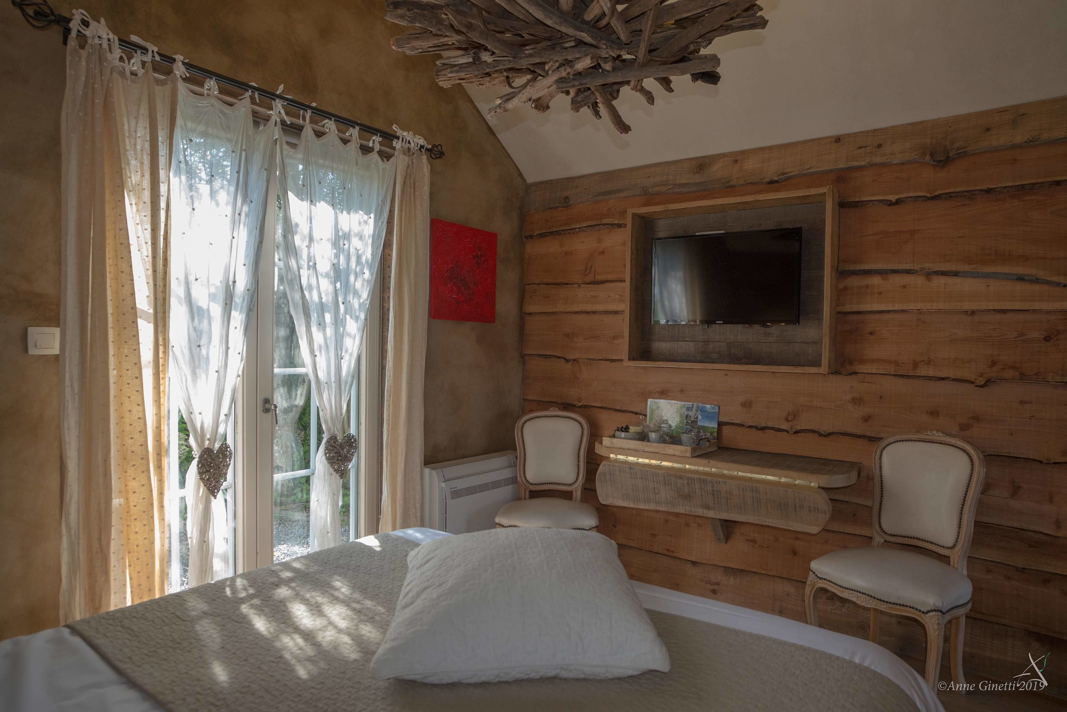 Een gezellige slaapkamer met een bed, twee stoelen, een kleine tafel en een televisie aan de muur.