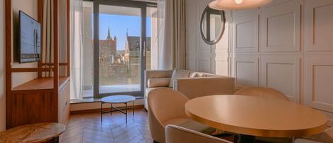 A modern hotel room with a large window, a round dining table, and a sofa.