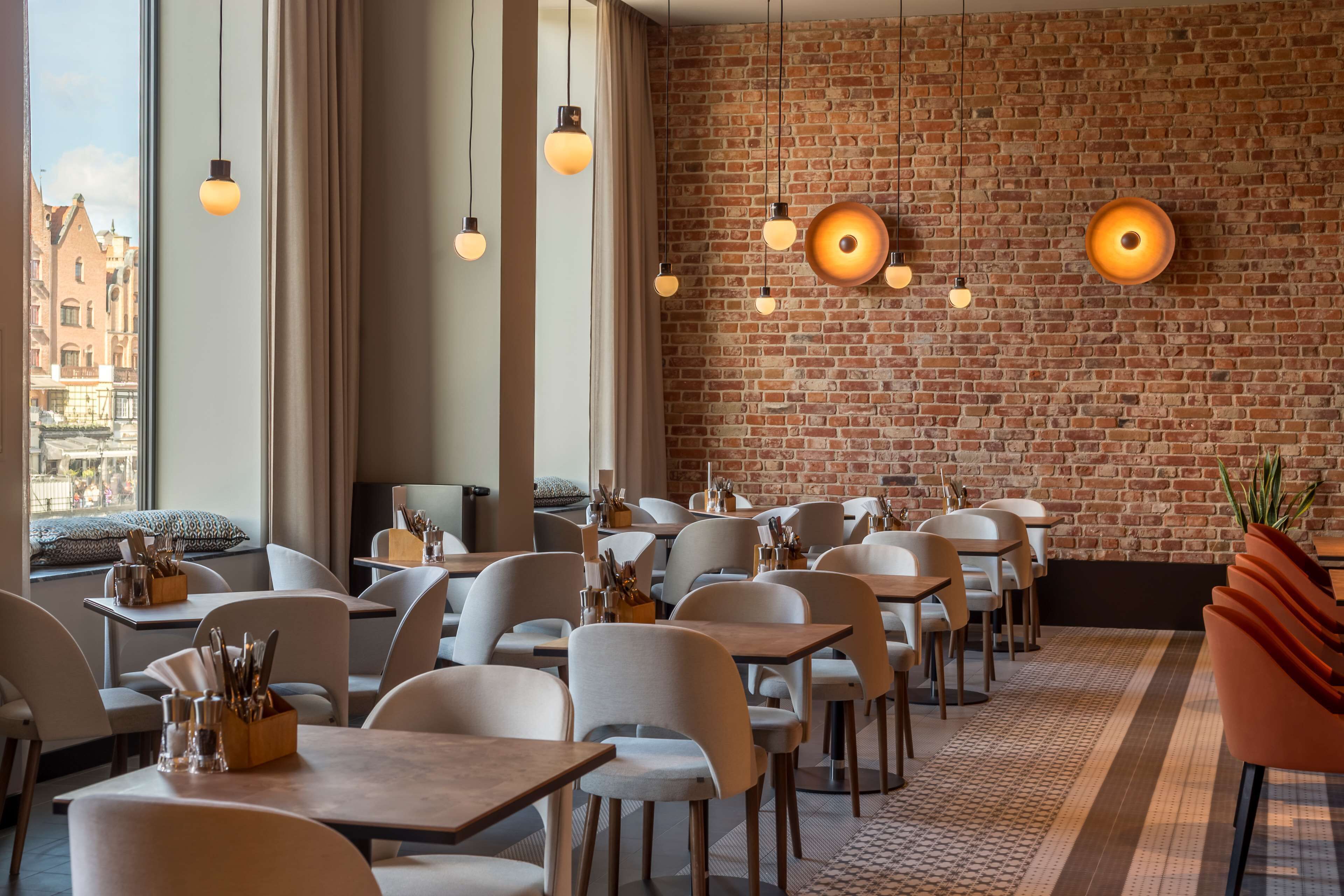 Un ristorante con pareti in mattoni, lampade a sospensione e vista sugli edifici circostanti.
