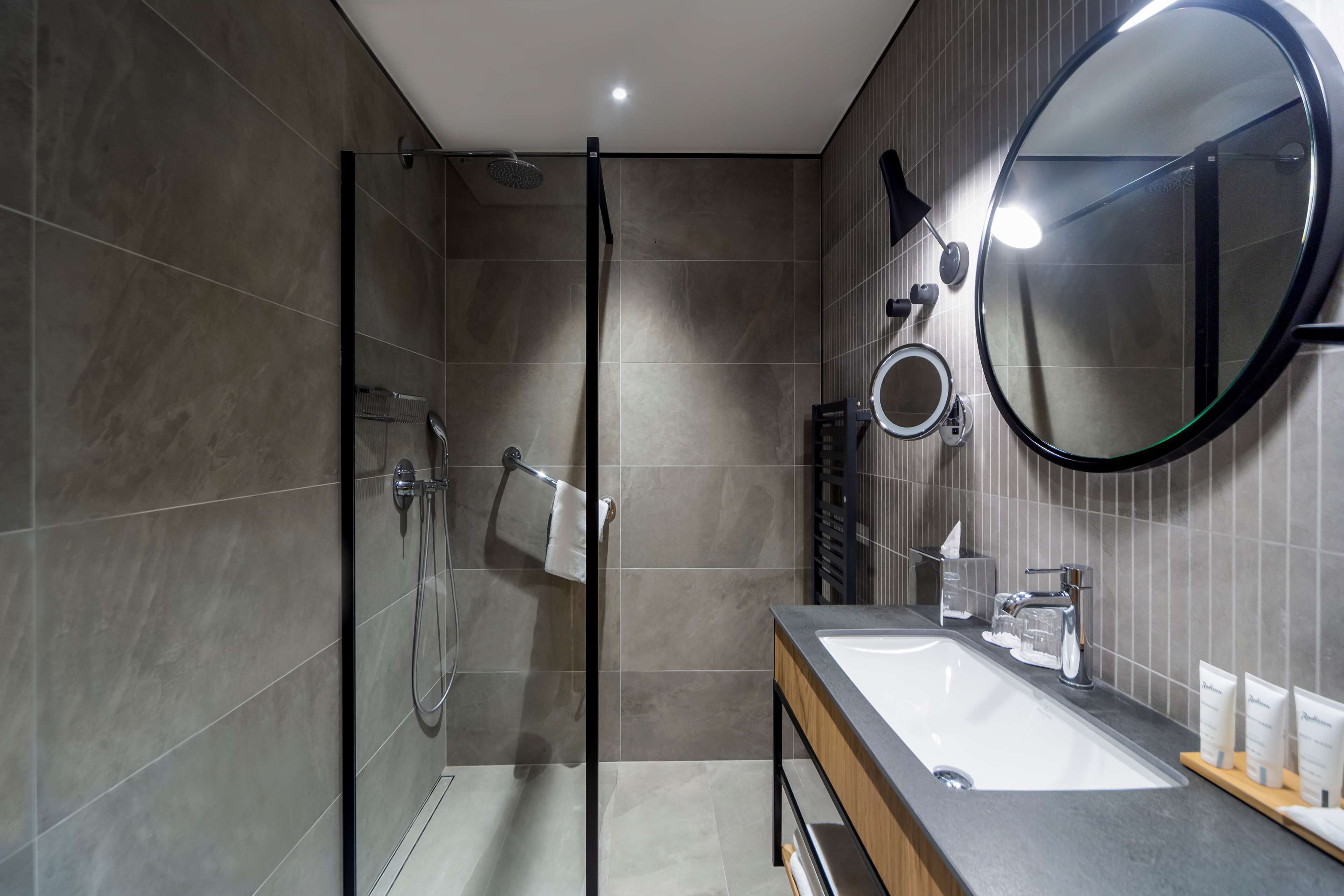 Un baño moderno con ducha de vidrio, un espejo grande y un tocador con lavamanos y encimera.