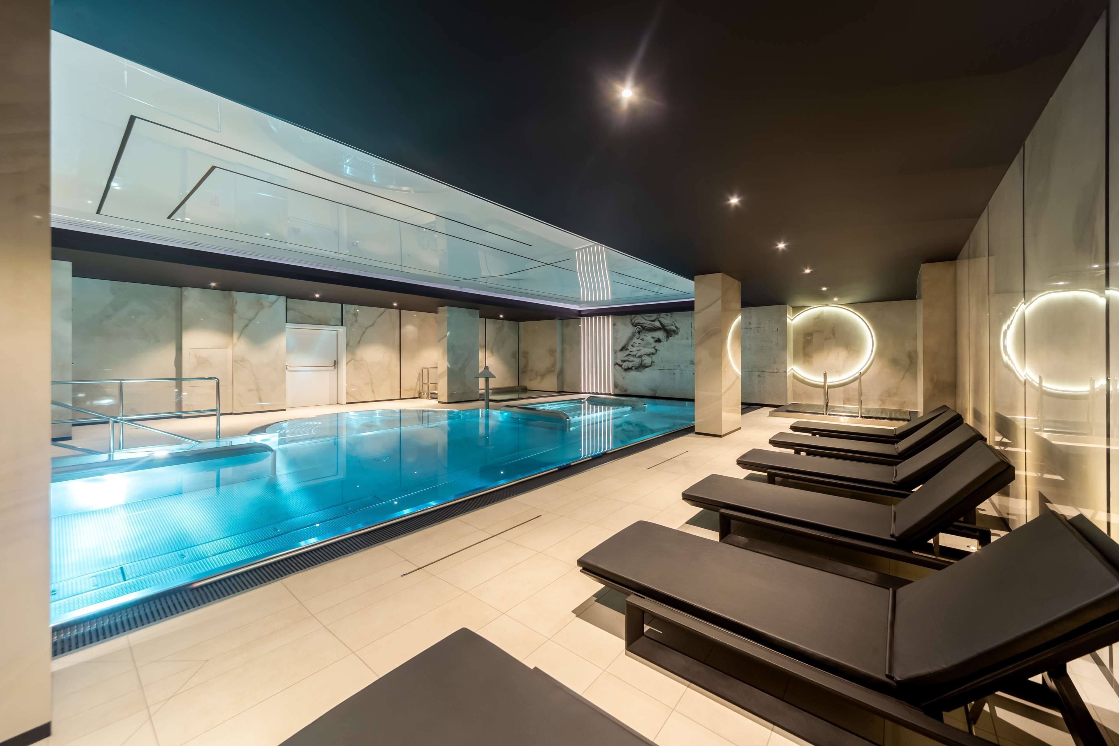 Ein moderner, überdachter Pool mit Glaswänden, Liegestühlen und minimalistischem Design.