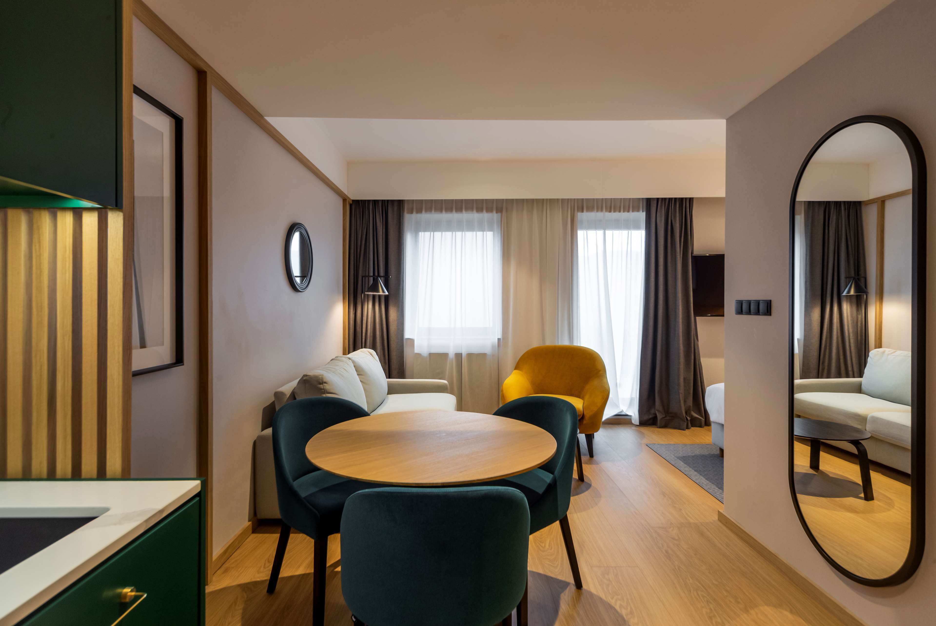 Una habitación de hotel con una mesa de comedor de madera, dos sillas, un sofá, un sillón amarillo y un espejo grande.