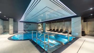 Ein moderner, überdachter Innenpool mit Glasdecke, Marmorwänden und Liegestühlen.