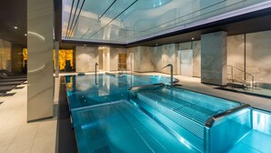En modern inomhuspool med väggar av genomskinligt glas, ett golv belagt med marmorplattor och en samtida design.