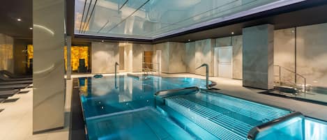 En moderne indendørs swimmingpool med vægge af glas, et marmortapet gulv og et tidssvarende design.
