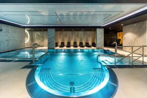 A modern indoor swimming pool with a glass ceiling, multiple seating areas, and a central water feature. - Radisson Hotel & Apartments Gdansk (Gdansk)