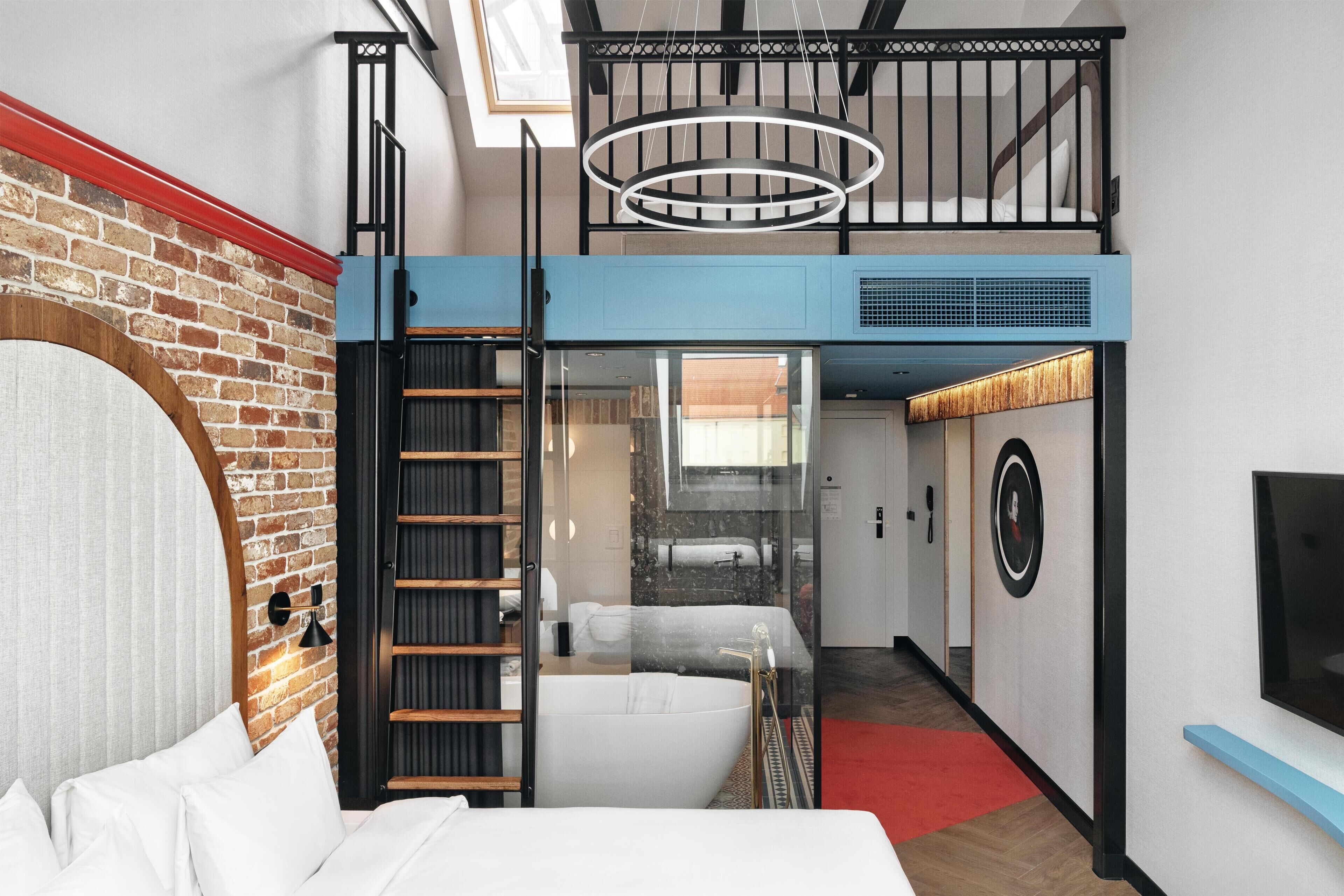 A modern hotel room with a loft-style design, including a balcony, a large bed, and a bathroom with a bathtub.