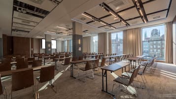 Et mødelokale med flere borde og stole, store vinduer med udsigt over byen og moderne loftdesign.