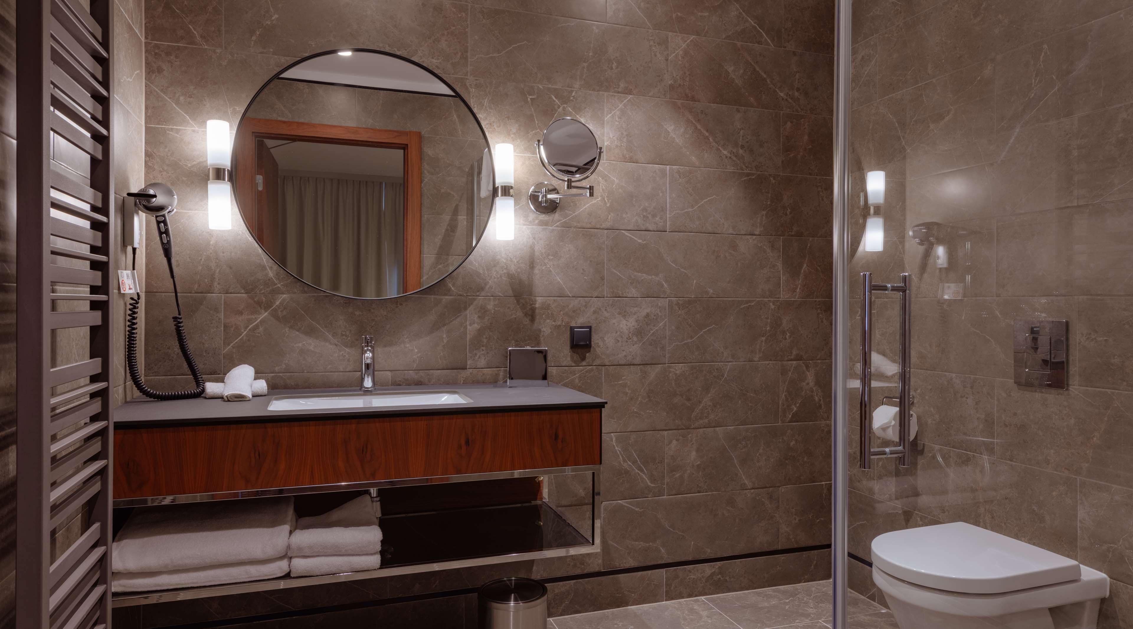 A modern bathroom with a marble-tiled shower, a wooden vanity with a sink, a mirror, and a toilet.