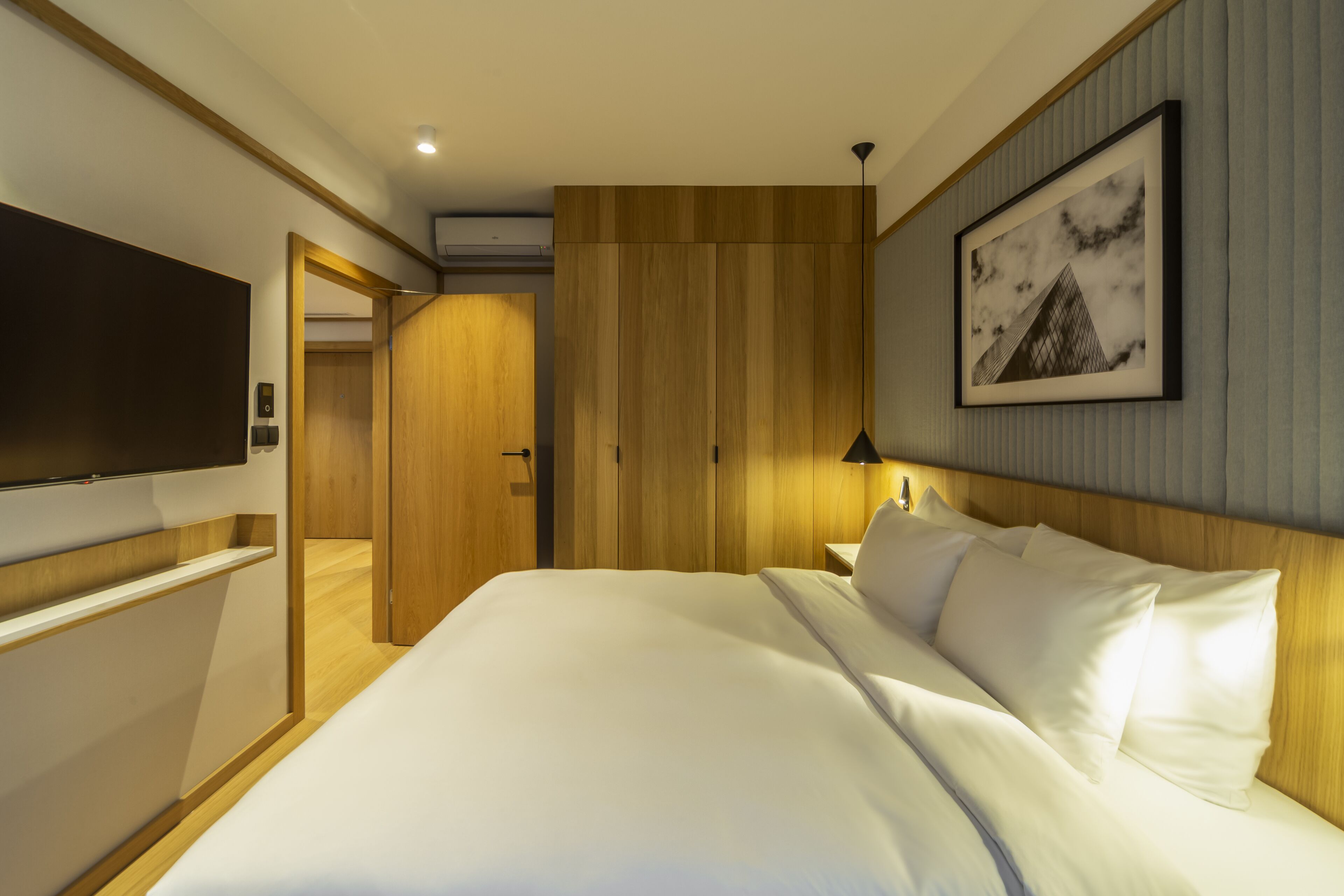 A hotel room with a large bed, a flat-screen TV mounted on the wall, a wooden headboard, and a framed picture on the wall.