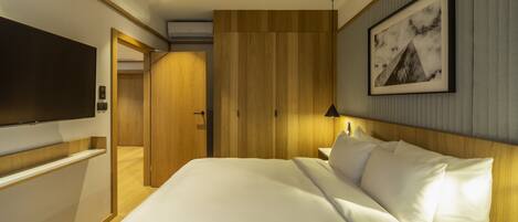 A hotel room with a large bed, a flat-screen TV mounted on the wall, a wooden headboard, and a framed picture on the wall.