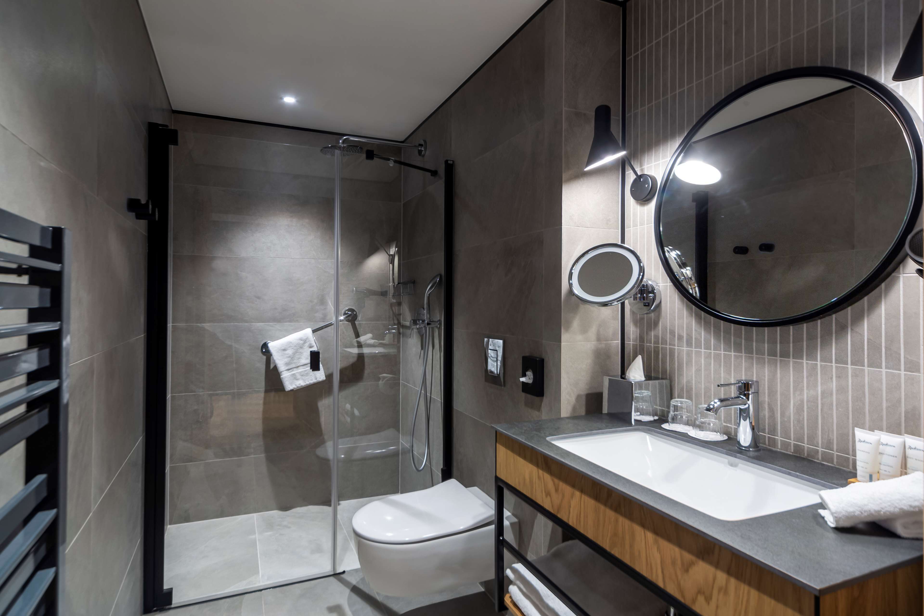Un baño moderno con ducha envuelta en vidrio, inodoro blanco, tocador con espejo y lavamanos.