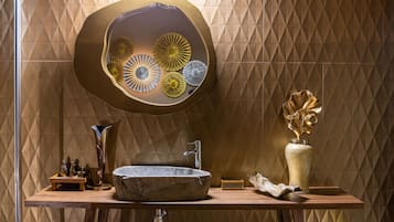 Une salle de bain avec un lavabo en pierre, un miroir orné d’assiettes décoratives, un vase et un mur à motifs géométriques.
