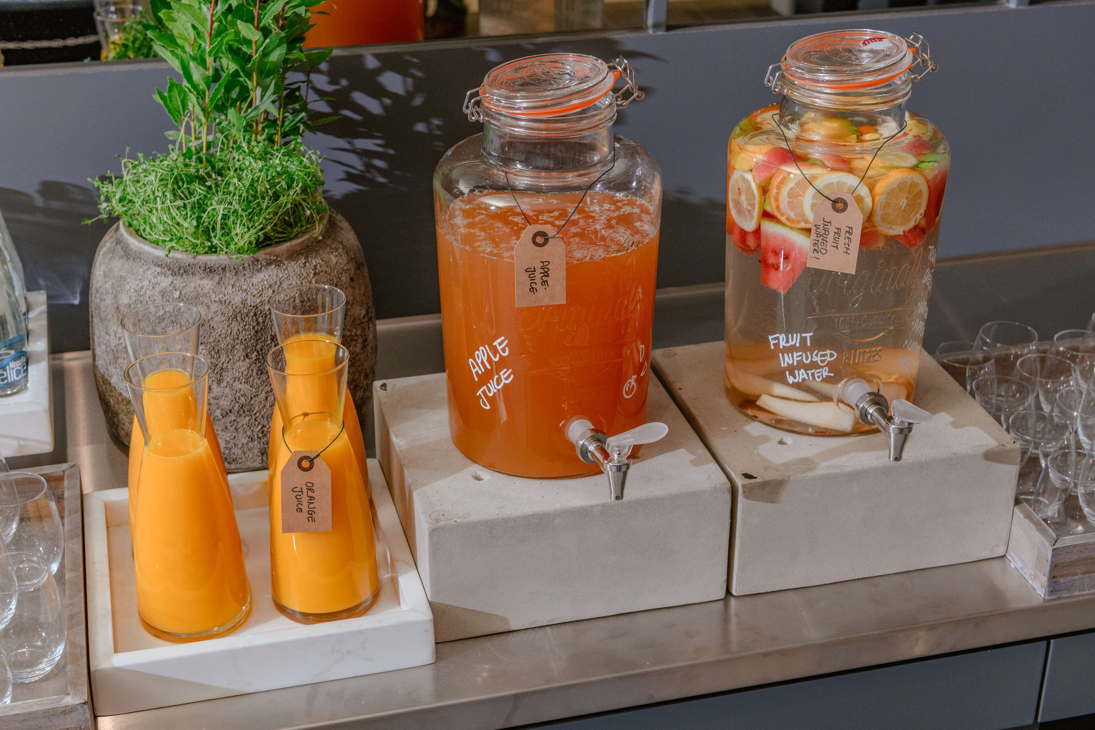 A beverage station with three dispensers: orange juice, apple juice, and fruit-infused water.