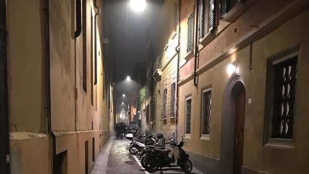 A narrow cobblestone street lined with buildings, some with balconies and shutters, and a few parked scooters. - Studio Hosts 2 Via Dè Ruini - Flat in Bo (Bologna)
