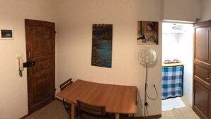 A room with a wooden table and chairs, a painting on the wall, a small kitchen area with a checkered tablecloth, and a door leading to another room. - Studio Hosts 2 Via Dè Ruini - Flat in Bo (Bologna)