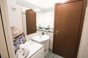 A bathroom with a white sink, wooden doors, a mirror, and a shelf with toiletries. - Studio Hosts 2 Via San Gervasio Flat in Bo (Bologna)