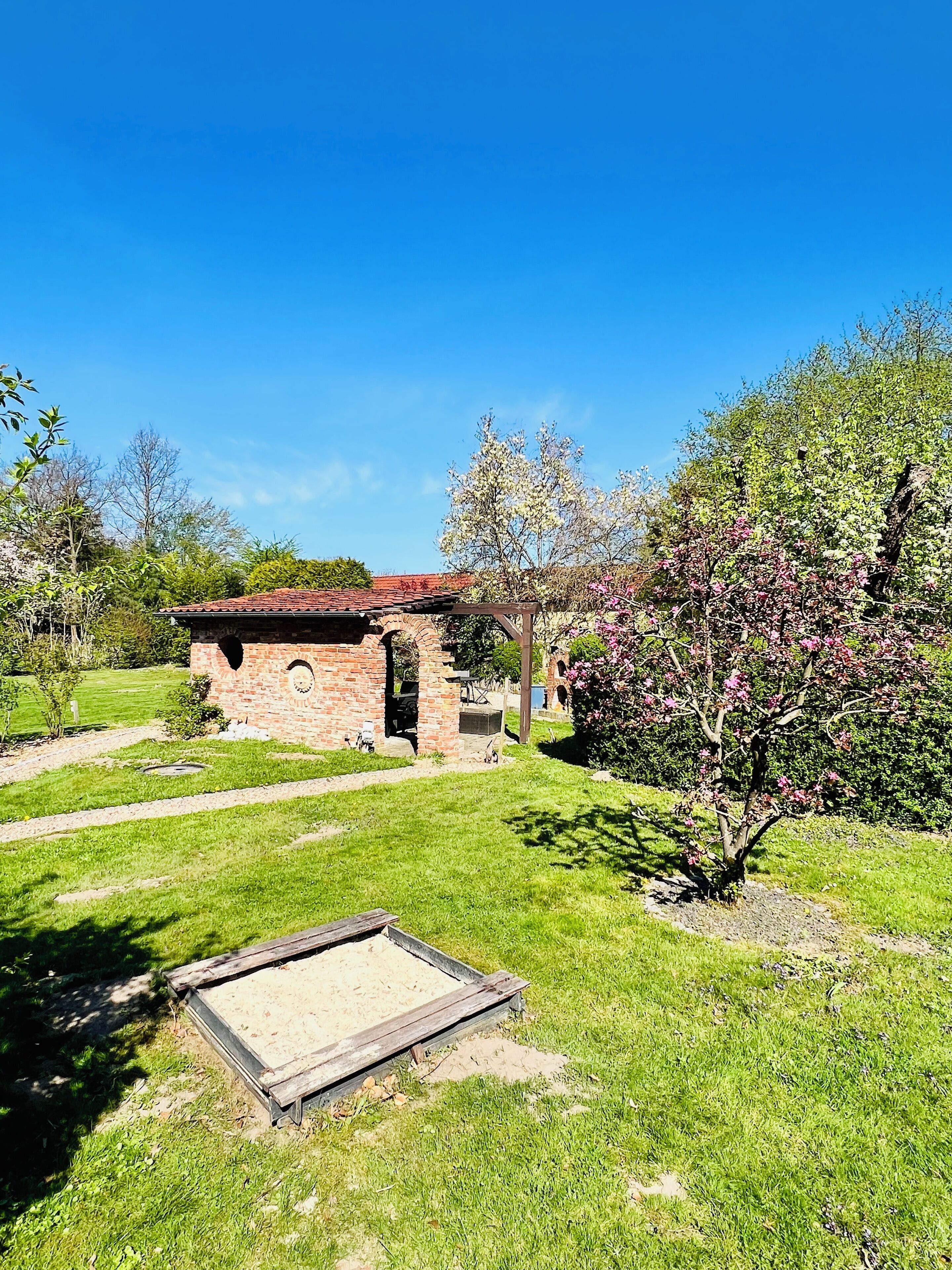 Un bâtiment en briques surmonté d’un toit rouge, entouré d’une pelouse bien entretenue et d’arbres en fleurs.