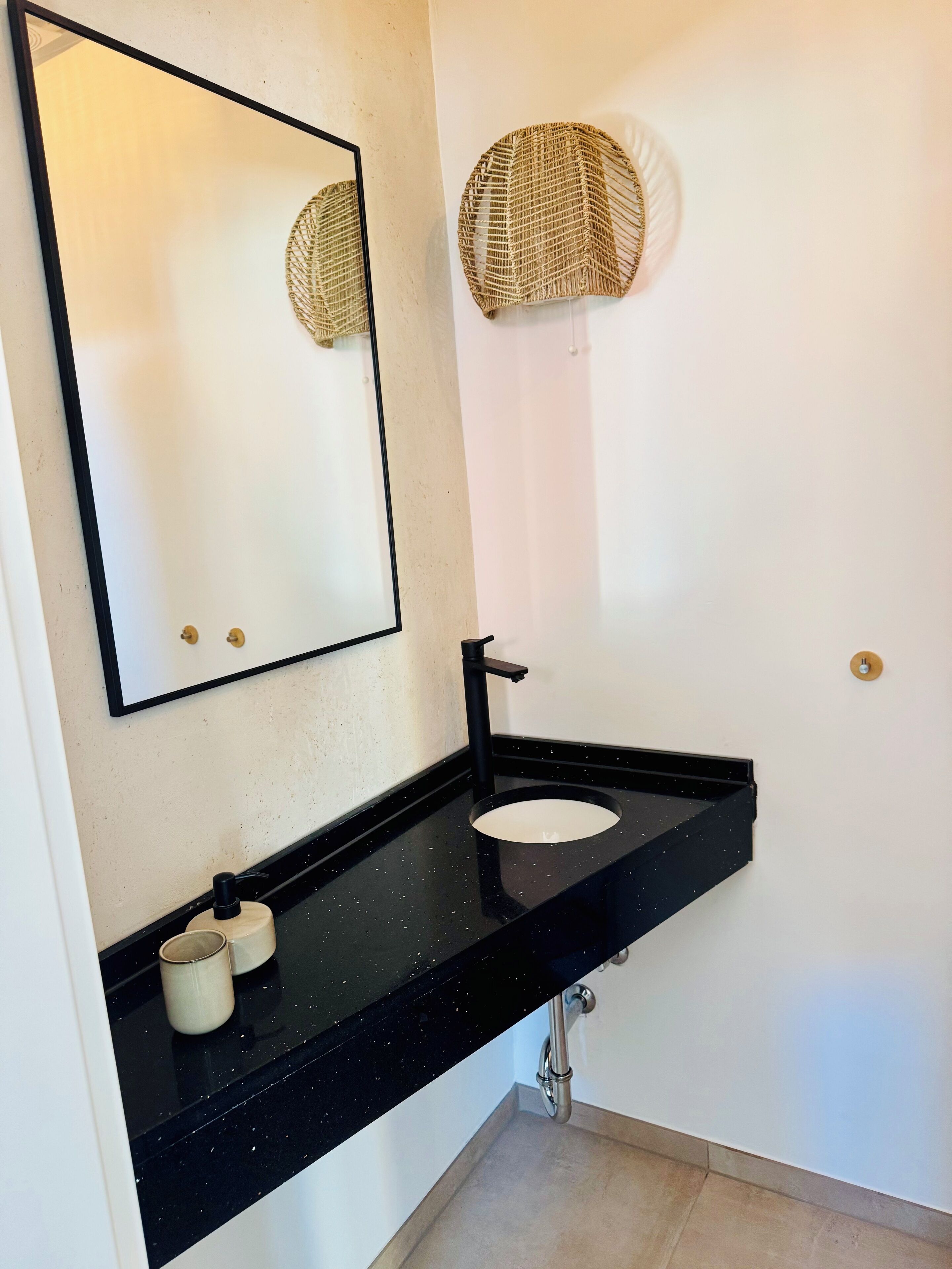 Une salle de bain moderne avec un plan de toilette noir, un lavabo rond, un miroir et un porte-serviettes fixé au mur.