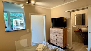 A hotel room with two beds, a TV, a wooden dresser, and a bathroom with a sink and mirror. - Ferienwohnung Maedchen (Wunstorf)