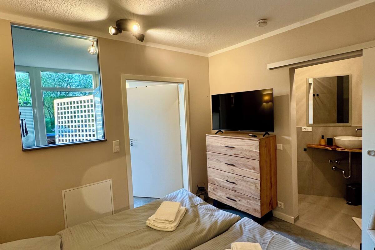 A hotel room with two beds, a TV, a wooden dresser, and a bathroom with a sink and mirror.