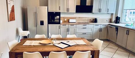 A modern kitchen with white cabinets, a wooden dining table, and a hanging light fixture.