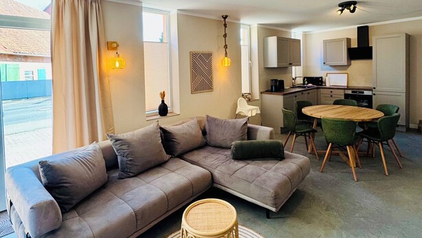 A modern living room with a sectional sofa, a round woven coffee table, and a dining area with a round table and chairs. - Ferienwohnung Maedchen (Wunstorf)