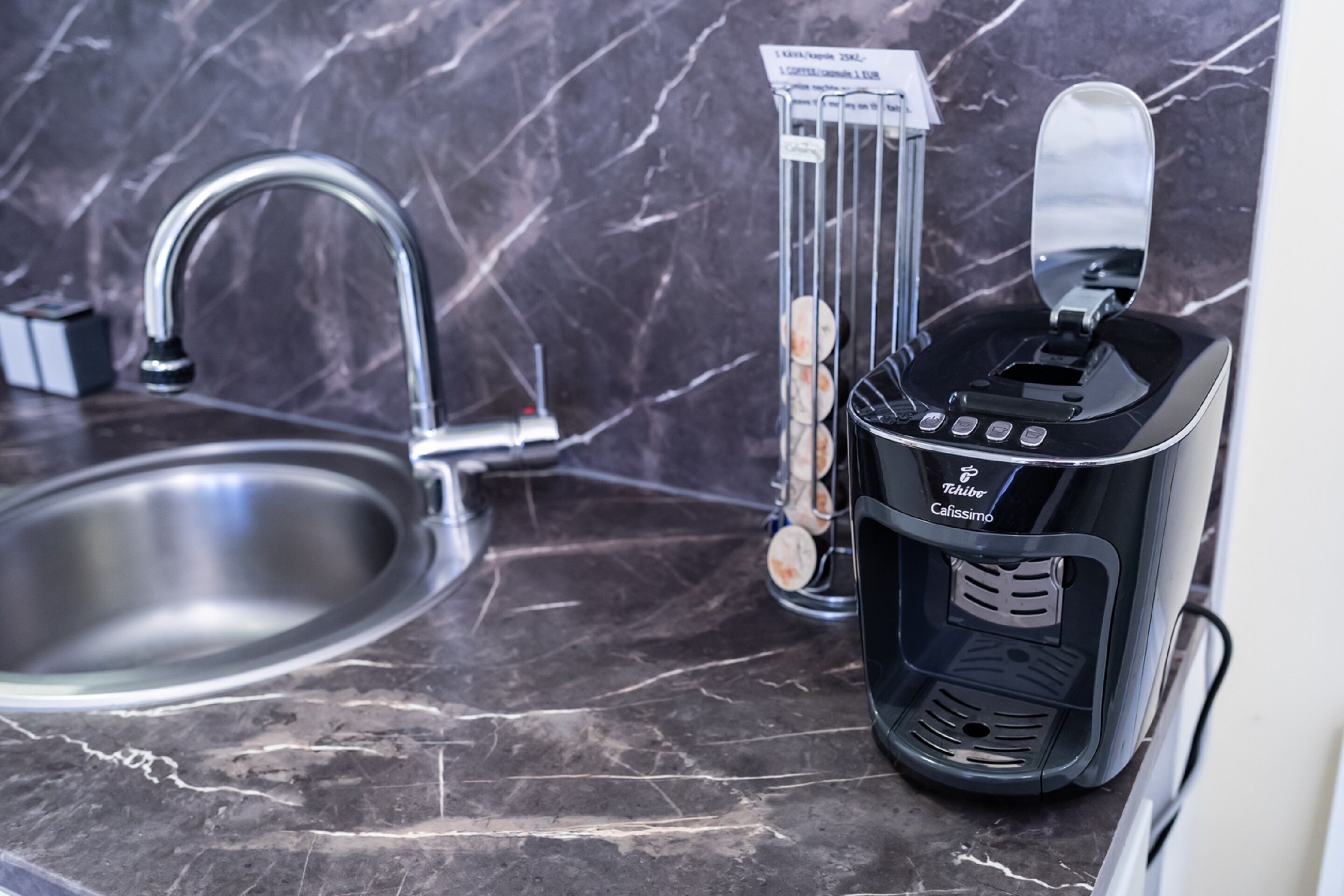 A kitchen with a modern faucet, a coffee machine, and a marble countertop.