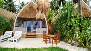 A thatched-roof bungalow with a wooden deck, two lounge chairs, a table, and a bench. - Karamba (Kizimkazi)