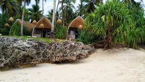 A beachside resort with thatched-roof huts, a rocky shoreline, and tropical vegetation. - Karamba (Kizimkazi)