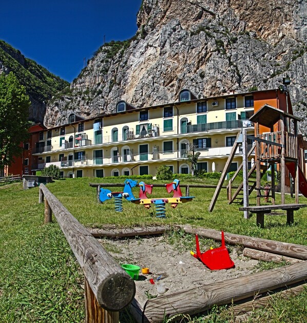 A playground with swings and slides, a wooden fence, and a building with balconies in the background.