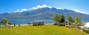 A lakeside view with a mountain in the background, a grassy area, and a small wooden structure.