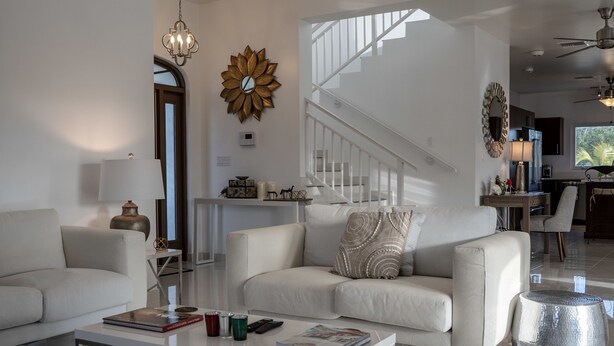 En moderne stue med en hvid sofa, et glasbord og en trappe, der fører op til et køkkenområde.