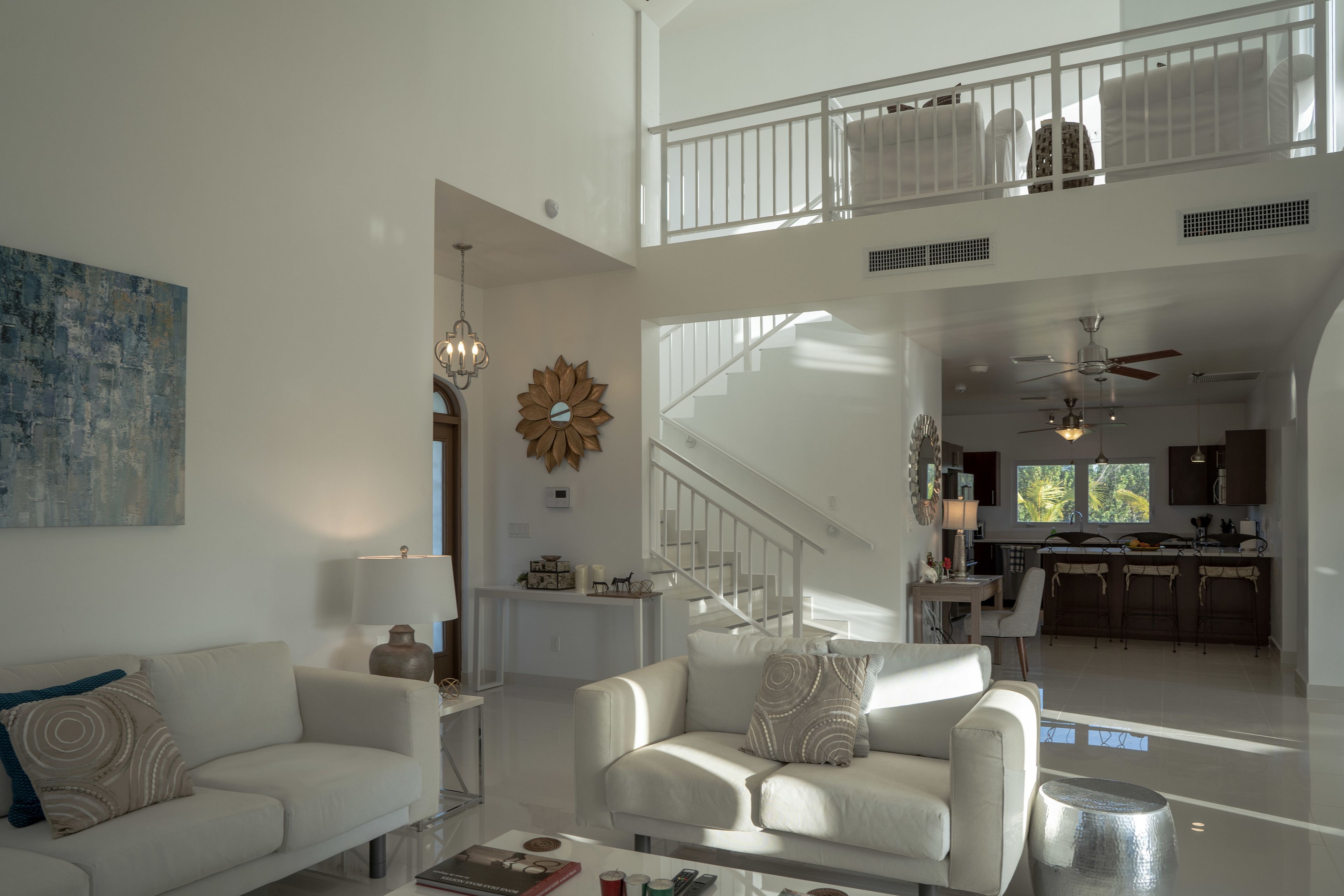Un vaste espace de vie doté d’un haut plafond, d’un escalier menant à un niveau supérieur et d’une cuisine ouverte sur le reste de la pièce.